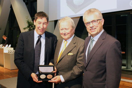 During the presentation Ralf Schumacher, Head of the Department for Finance and Economy, (left) gives the medal to Dr. Wolfgang Posche. On the right Peter Huber, Director of the State Mints of Baden-Wuerttemberg.