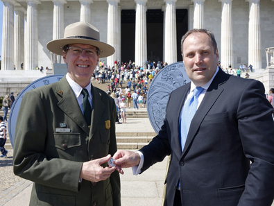 U.S. Mint Principal Deputy Direct Rhett Jeppson passes a 100th Anniversary National Park Service Commemorative Coin to Victor Knox, National Park Service Associate Director for Park Planning, Facilities, and Lands. The second of two commemorative coin programs for 2016, surcharges from the sale of the coins have been authorized to be paid to the National Park Foundation. U.S. Mint photo by Sharon McPike.