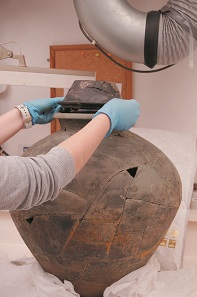 British Museum conservator Kathleen Magill placing the lid of the Frome hoard onto the Frome hoard pot. © The Trustees of the British Museum.