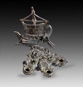 Lot 234: Oceanus-shaped bronze lamp with attachment in the shape of a ship. Roman, 1st-2nd cent. AD. From the Shlomo Moussaieff Collection. With export permission from the Israel Antiquities Authority. Estimate: 50,000,- euros. From Gorny & Mosch sale 248 (June 30, 2017), No 234