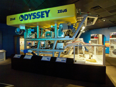 Visitors observe the life-size replica of the eight-ton Remotely Operated Vehicle (ROV) ZEUS. The ROV is fitted with high-definition still and video cameras and lights, and can descend to the ocean floor at depths of over 8,000 feet. Photo: Odyssey Marine Exploration, Inc., www.shipwreck.net.